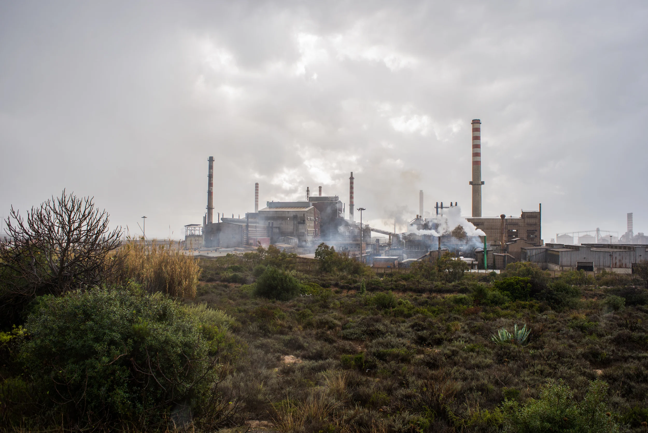 La Portovesme srl del gruppo svizzero Glencore, colosso mondiale per le materie prime, produce zinco e piombo estraendoli dai fumi di acciaieria, cioè dagli scarti di lavorazione dell'acciaio. Il cuore dell'impianto della Portovesme sono i forni Waeltz che consentono un doppio profitto: estrarre materia prima da trattare e poi rivendere, e smaltire gli scarti provenienti da altre acciaierie d'Italia e spesso dall'estero. Come testimonia il caso inquietante del 2012, che fece scattare l'allarme radioattività per la presenza di Cesio 137 nei sacchi di fumi di acciaieria su un carico arrivato via mare dalla Grecia. Dai fumi d'acciaieria la percentuale di recupero della Portovesme Srl è solo del 25%; il restante 75% - scarto dello scarto - è composto da rifiuti tossici di cui disfarsi, nell'ormai colma discarica di Genna Luas. Grazie a interventi legislativi, in contrasto con le normative europee, in Italia i rifiuti speciali che entrano in un ciclo produttivo vengono classificati materie prime secondarie. 