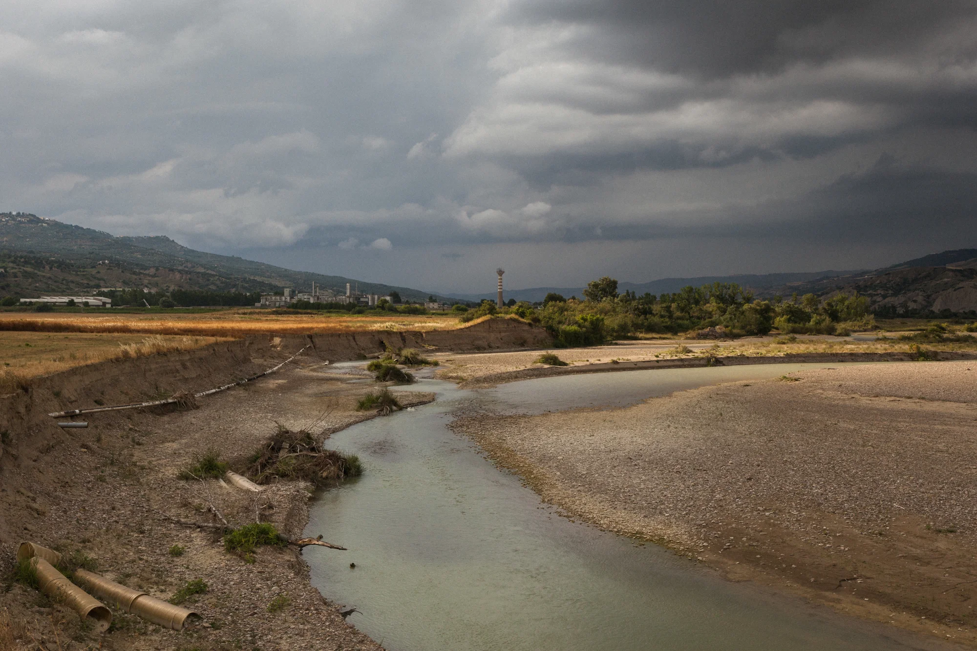 Il fiume Basento, sullo sfondo l’area industriale di Ferrandina (MT), 2015. Il fiume scorre tra i campi coltivati a grano e l’area industriale, per poi sfociare nel mar Ionio. Indagini dell’ARPA Basilicata ne hanno evidenziato lo stato critico: sono presenti sostanze nocive e cancerogene, tanto nelle acque superficiali quanto in quelle profonde. 