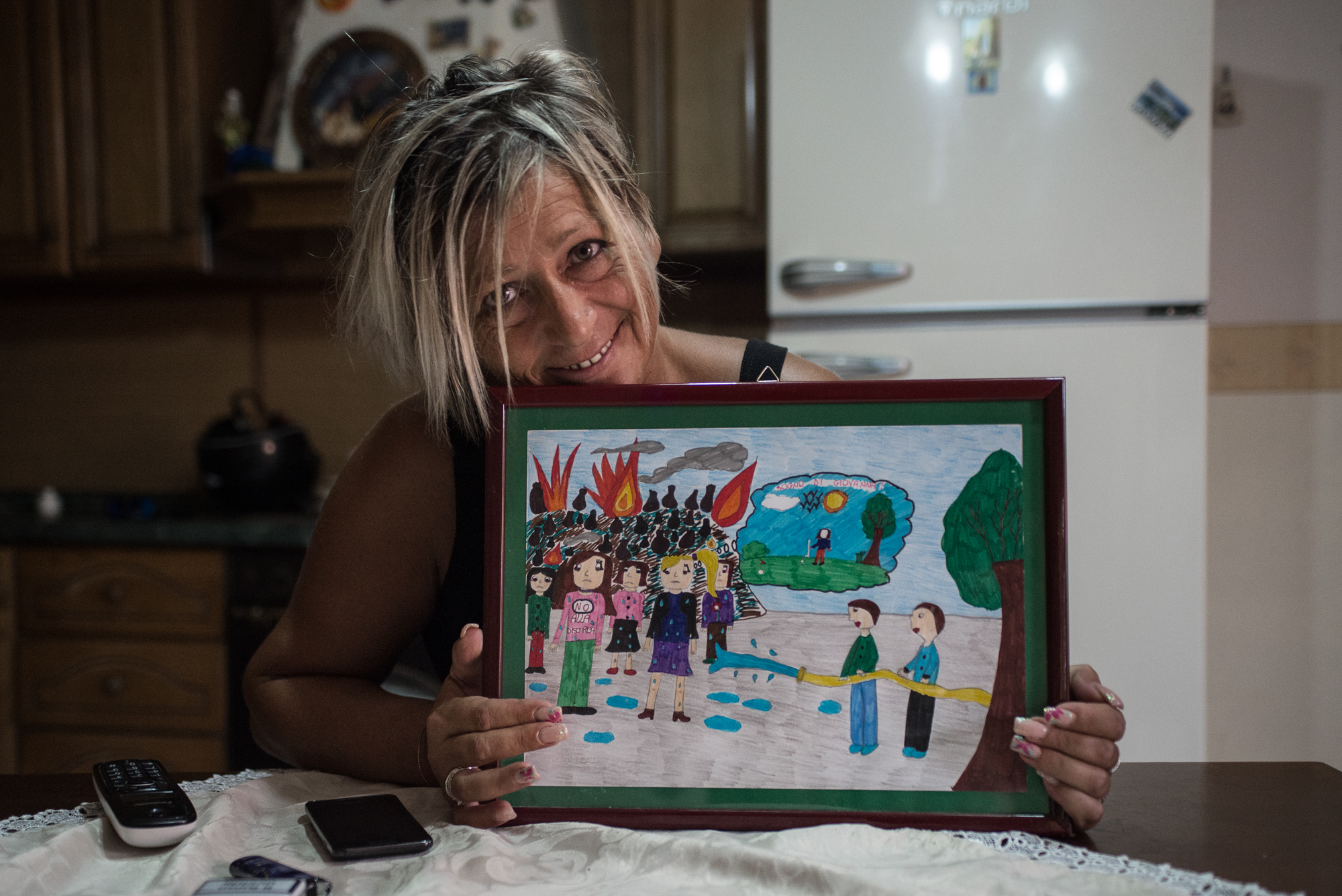  Pianura, (NA), 2015. Giovanna, 45 anni, residente a Napoli, nel quartiere di Pianura. Reduce da diverse patologie tumorali sconfitte e con altre patologie in via di sviluppo, mostra un disegno degli alunni della scuola elementare in cui ha lavorato.