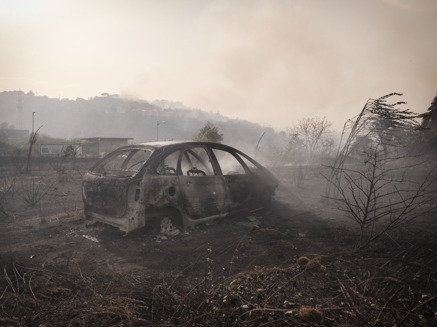  I resti di una macchina incendiata nei pressi di Aci Catena. Nello sfondo solo visibili i fumi degli incendiprovenienti dal comune di San Nicolò. 