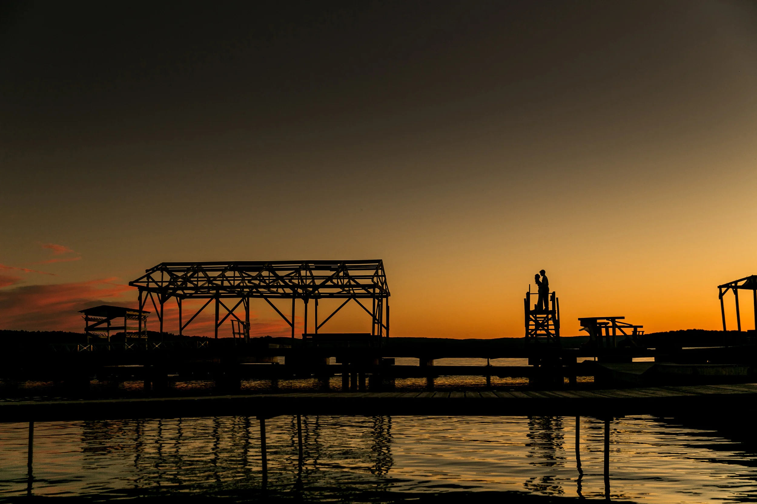 Bride and groom silhouette portrait during sunset on a lakeside dock