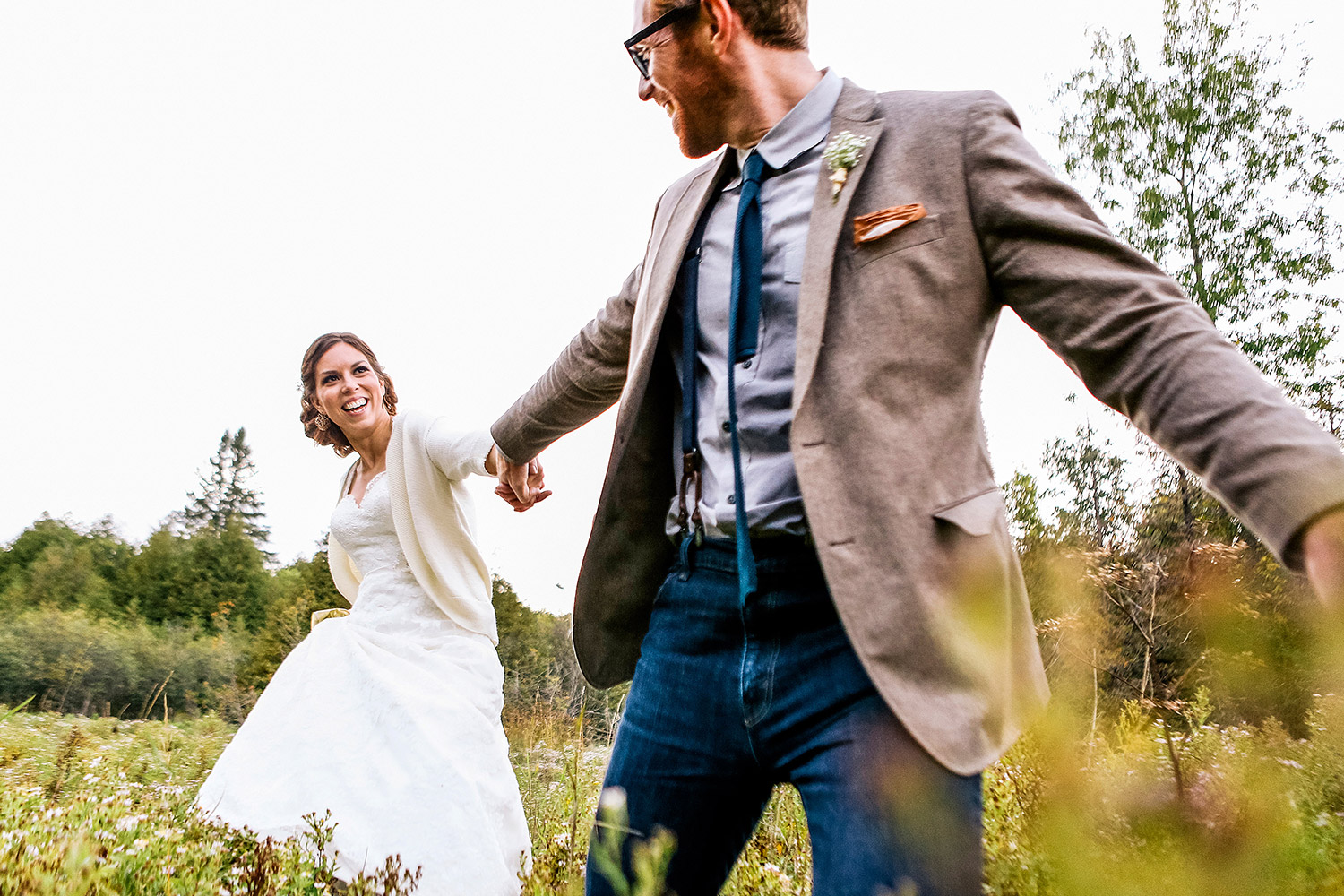 Bride and groom running hand in hand though a field during a wedding at the Herb Garden in Almonte Ontario