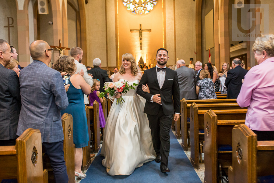 smiling-bride-and-groom-walking-down-church-aisle-as-husband-and-wife-after-ottawa-wedding-ceremony