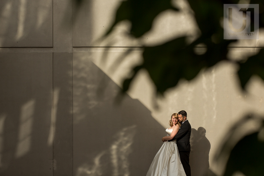 bride-groom-in-back-to-chest-embrace-in-front-of-concrete-wall-downtown-ottawa