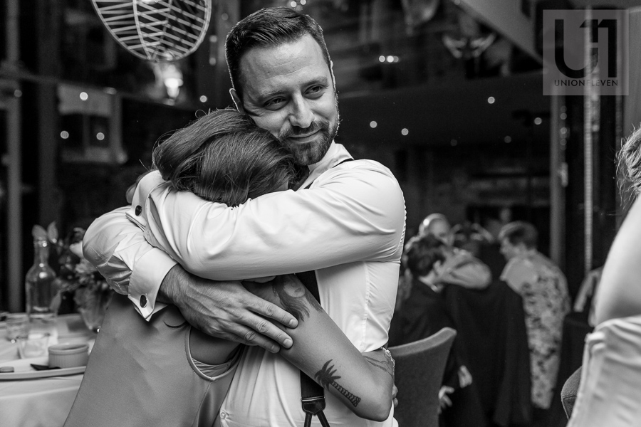 black-and-white-image-of-groom-hugging-bridesmaid-during-wedding-reception-at-eighteen-restaurant-in-ottawa