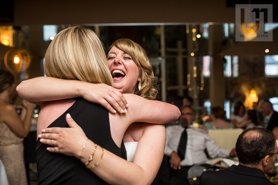 bride-smiling-and-hugging-female-guest-during-wedding-reception-at-eighteen-restaurant-in-ottawa