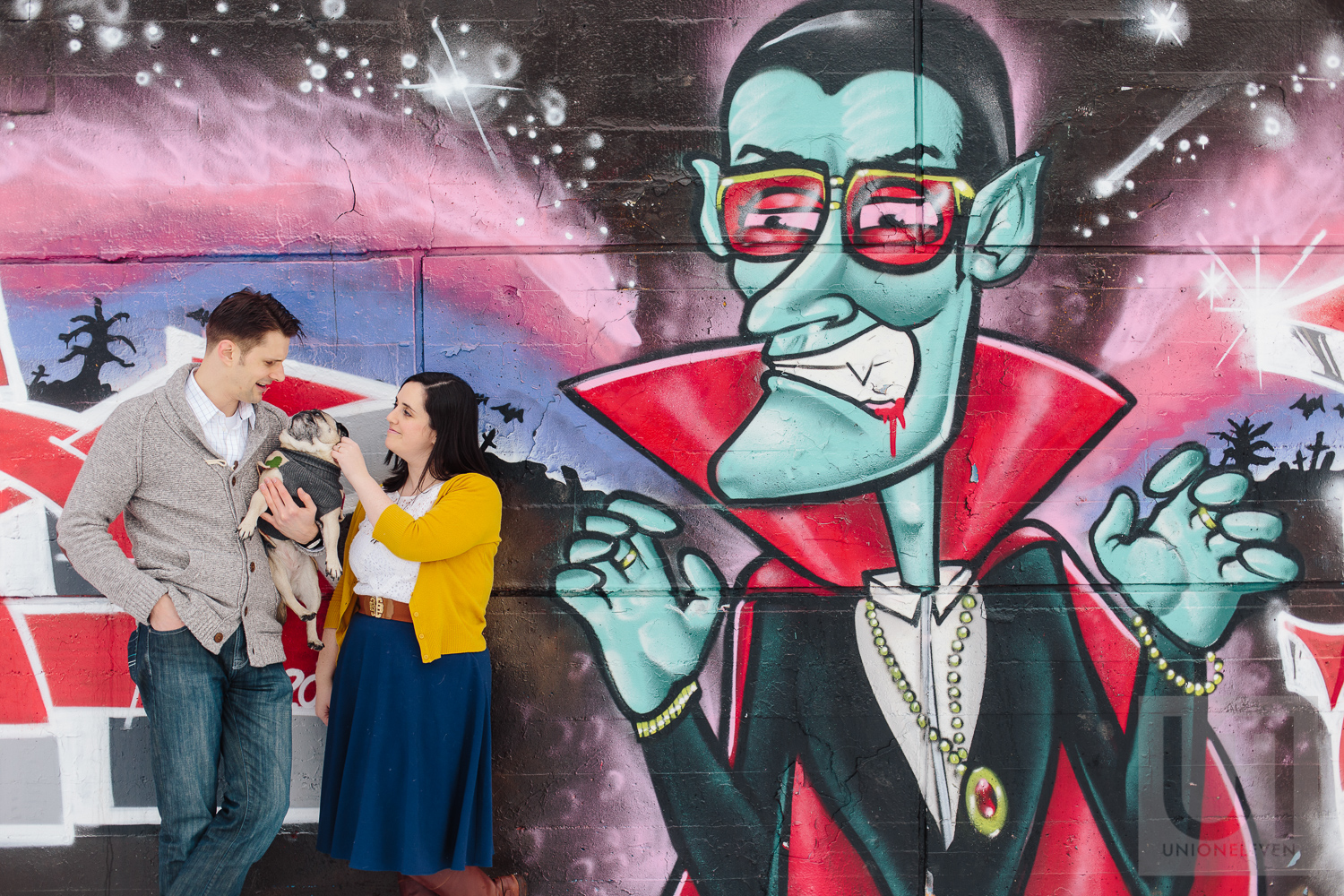 Engagement shoot with the couple and their pug in front of a graffiti wall in Ottawa