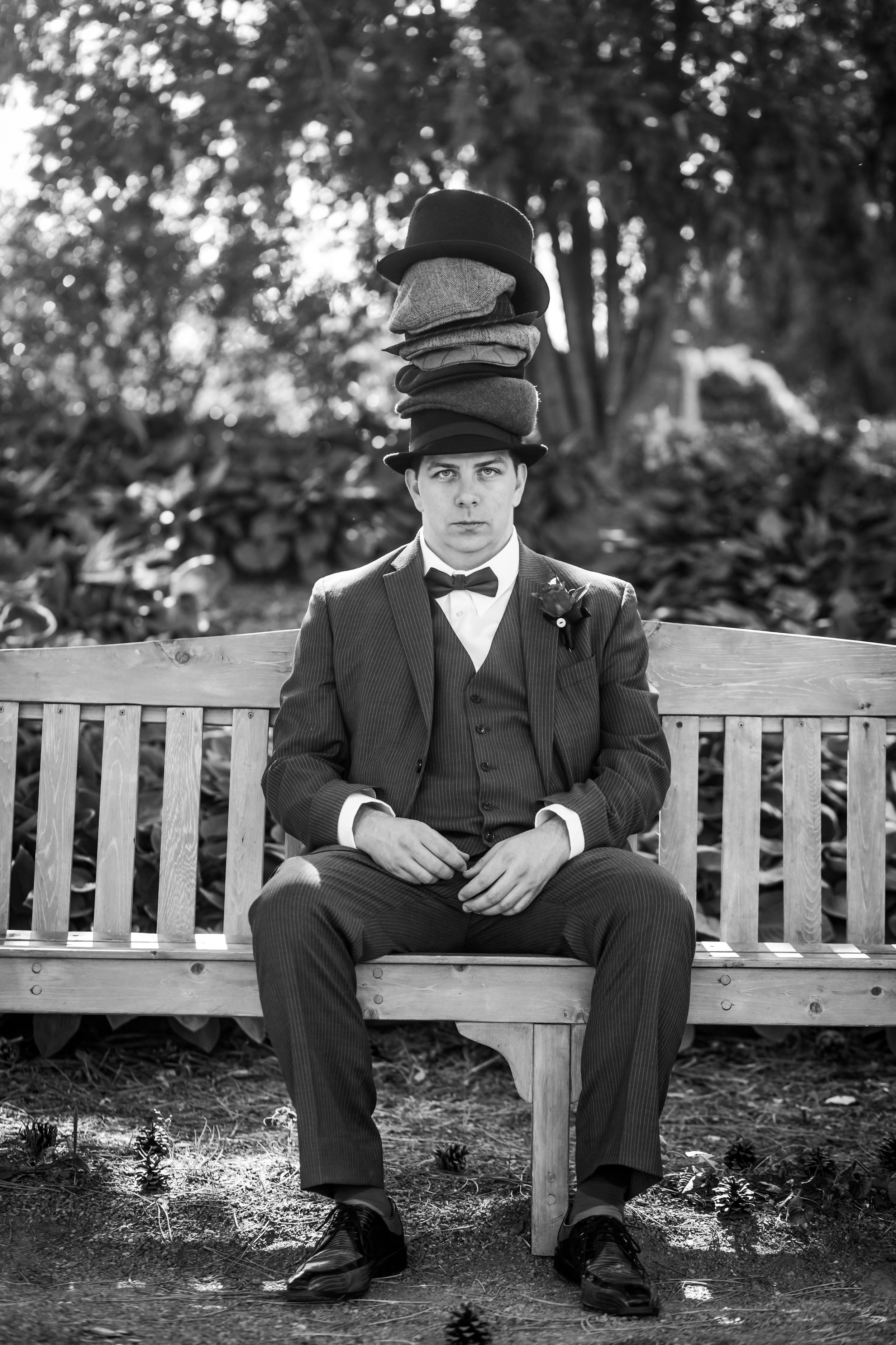 A portrait of the groom seated on a bench wearing a bunch of hats