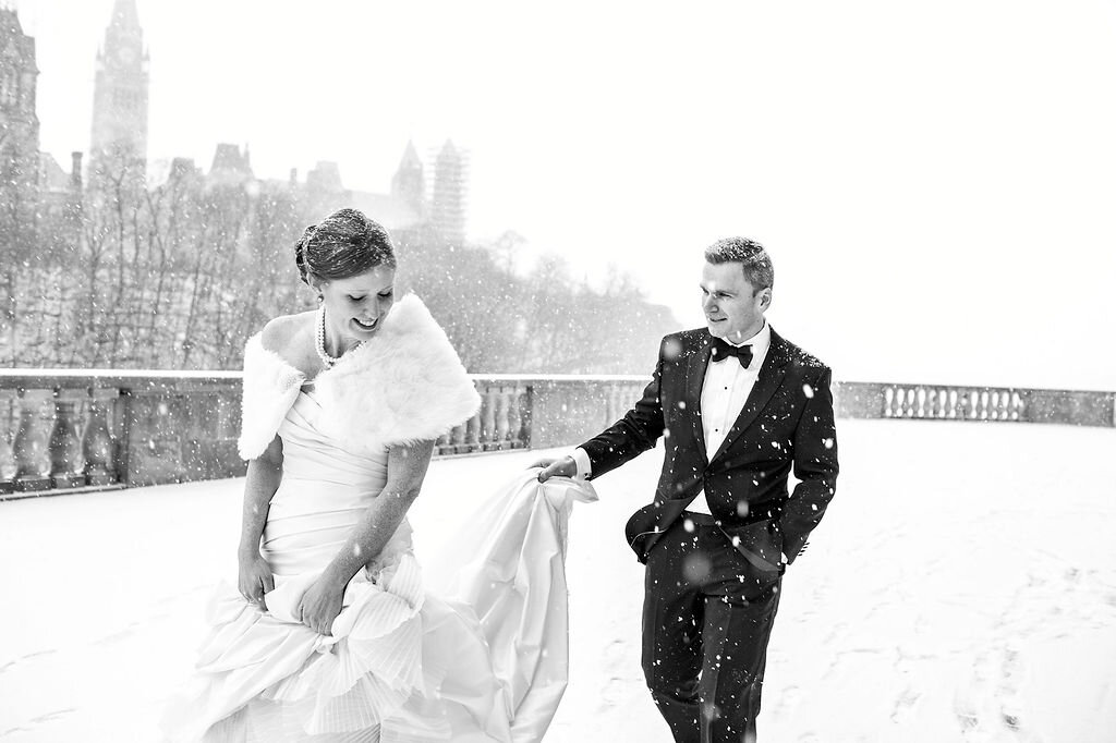 groom holding bride's wedding dress train on a snowy day outside the chateau laurier