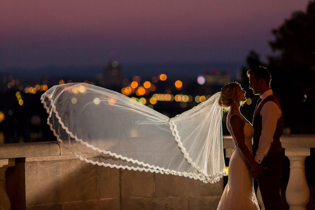 bride and groom holding hands on Chateau Laurier terrace at night while bride's veil blows in the wind