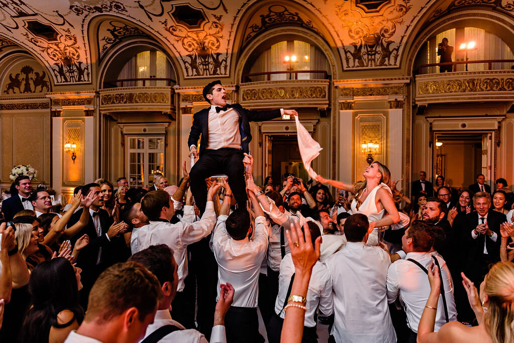 groom and bride being hoisted into the air on chairs by wedding guests inside Chateau Laurier ballroom 