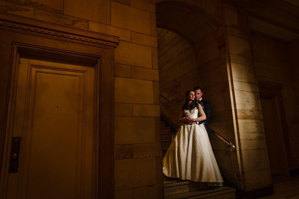 portrait of bride leaning into groom's embrace in staircase at Ottawa's Chateau Laurier
