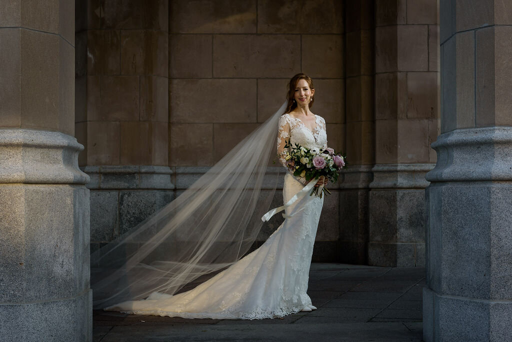portrait of bride with long veil holding her bouquet in front of Ottawa Chateau Laurier