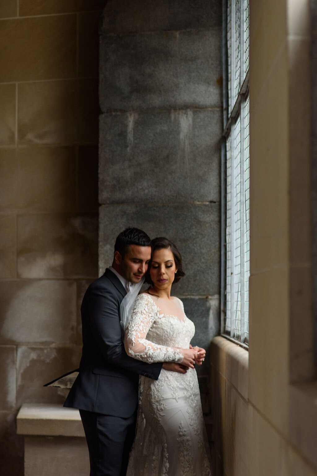 Groom embracing bride from behind while standing in front of a window near Chateau Laurier in Ottawa