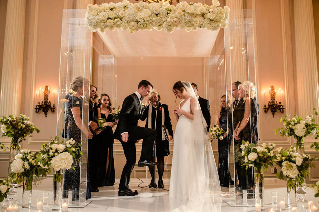 Jewish groom breaking the glass while bride and wedding party look on during Chateau Laurier wedding ceremony