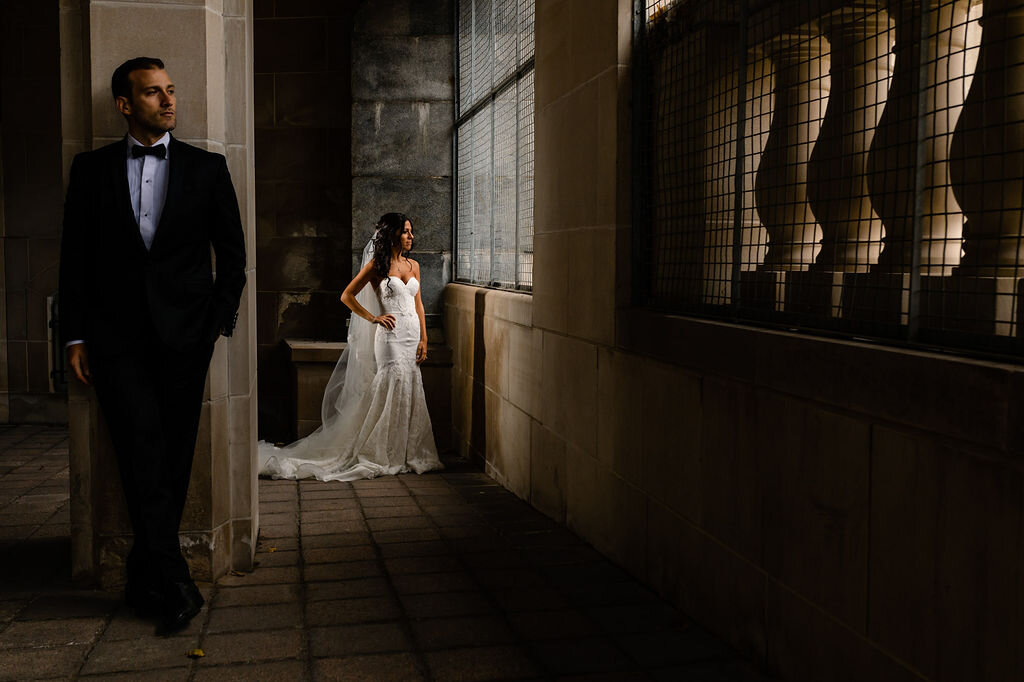 stylish portrait of groom leaning against stone wall and bride facing a window near Ottawa Chateau Laurier