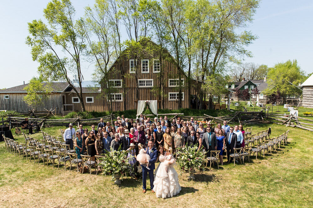 Photograph of a couple and all their wedding guests taken in front of a barn at Stonefields Estate near Ottawa
