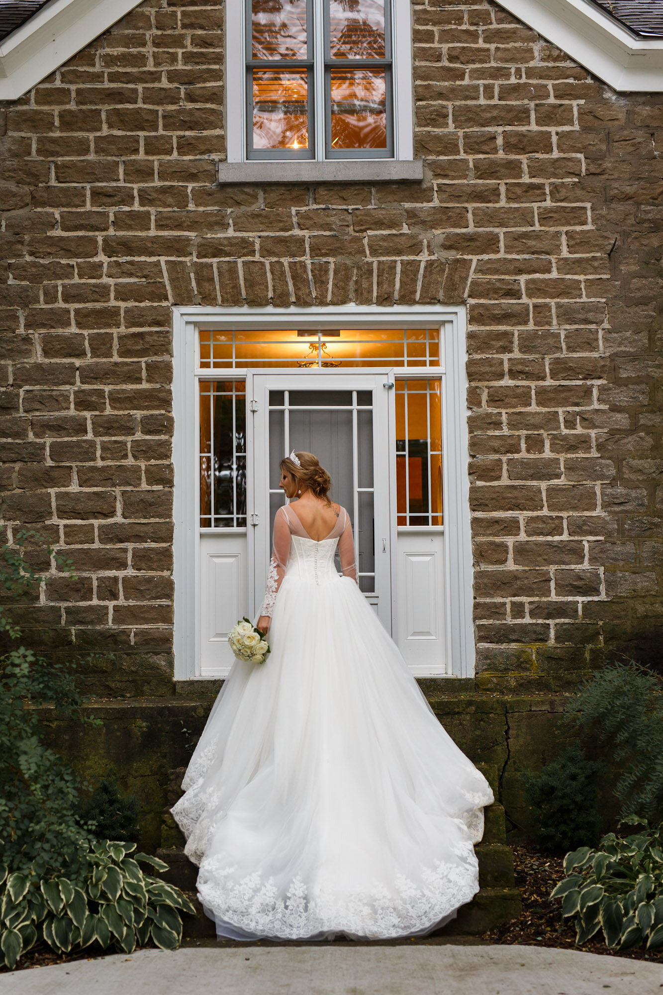 Portrait of bride taken from behind in front of stone house at Stonefields Estate near Ottawa