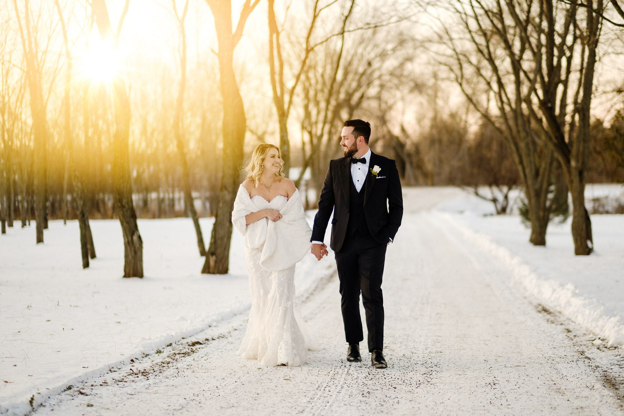 Couple walking down a snow covered road lined with trees at Stonefields Estate