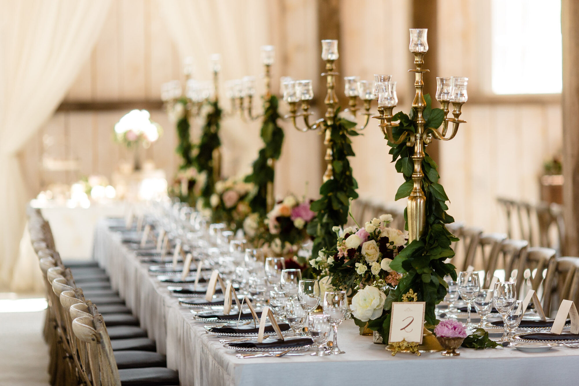 Wedding tablescape featuring candelabras covered in greenery and place settings on a harvest table 