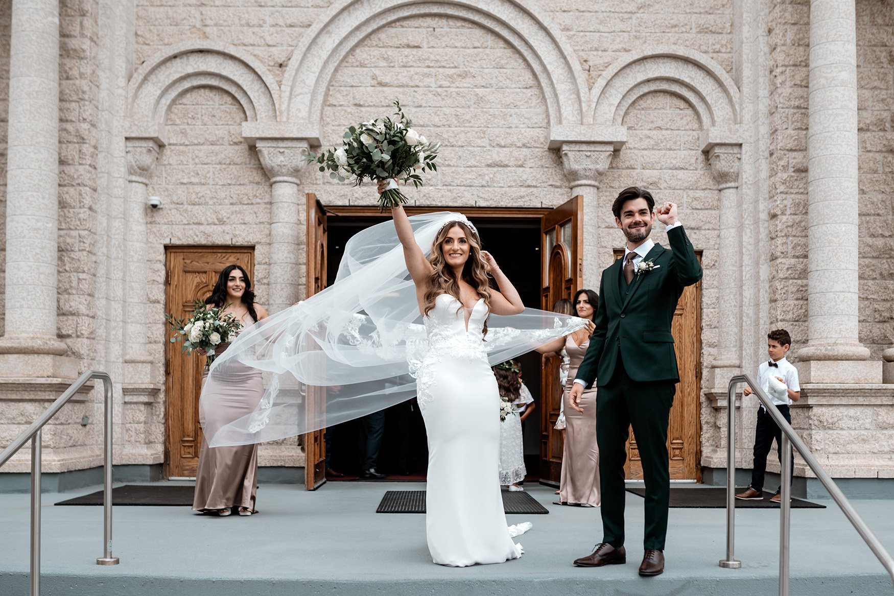 bride and groom celebrate with fist pumps outside saint elias church after wedding ceremony in ottawa ontario