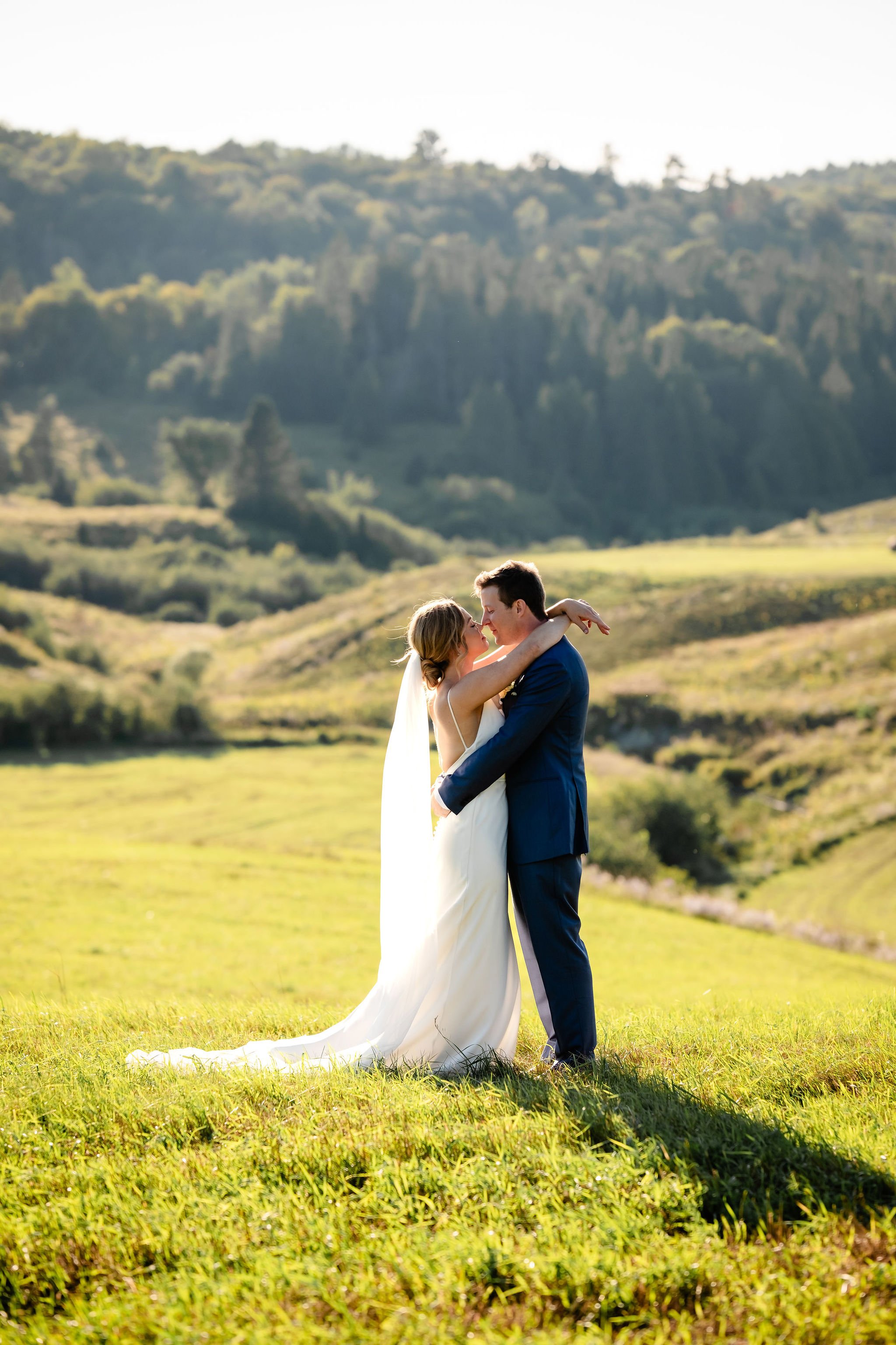 natural light photograph of a bride and groom in front of an expansive field as the sun sets behind them