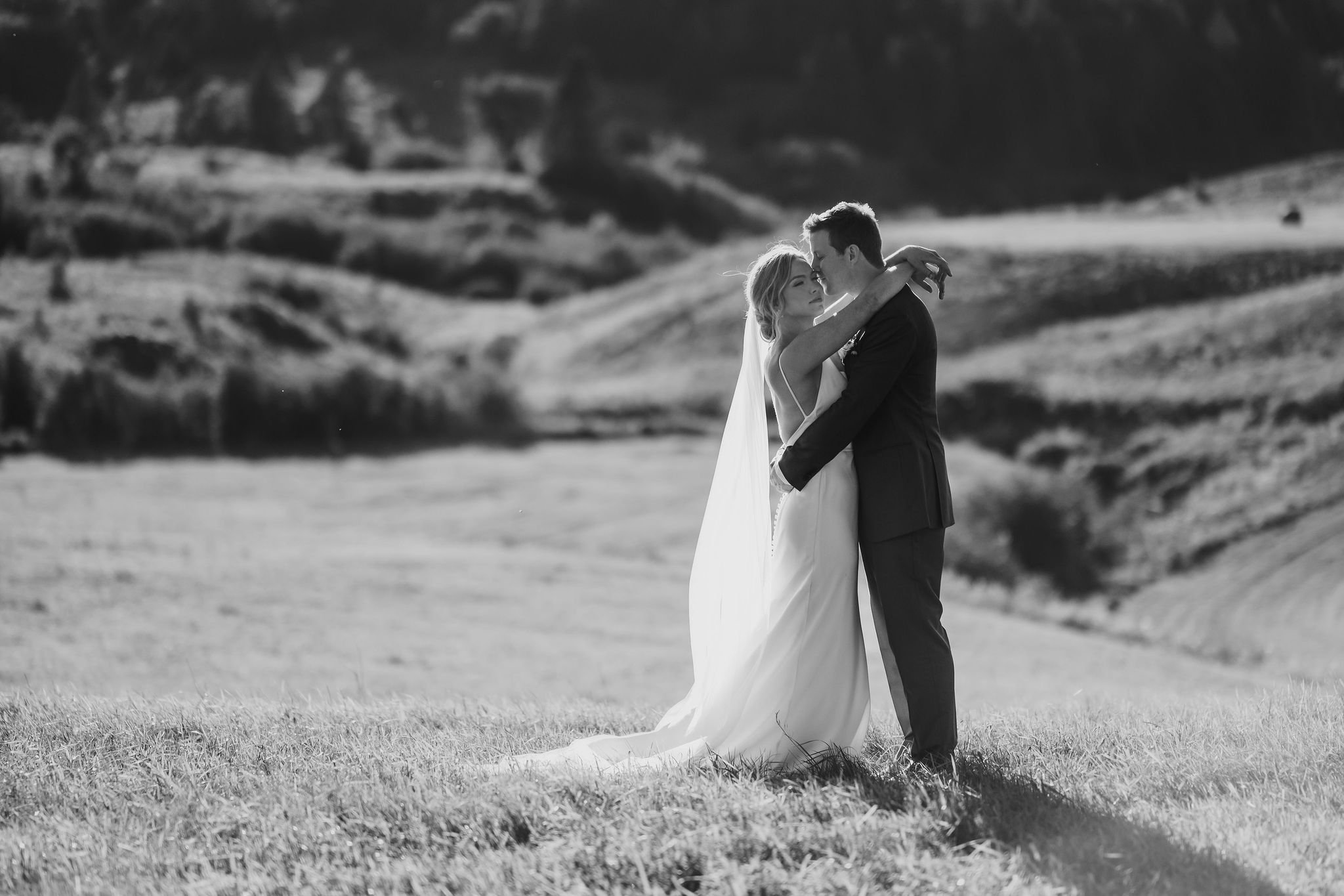 natural light photograph of a bride and groom in front of an expansive field as the sun sets behind them