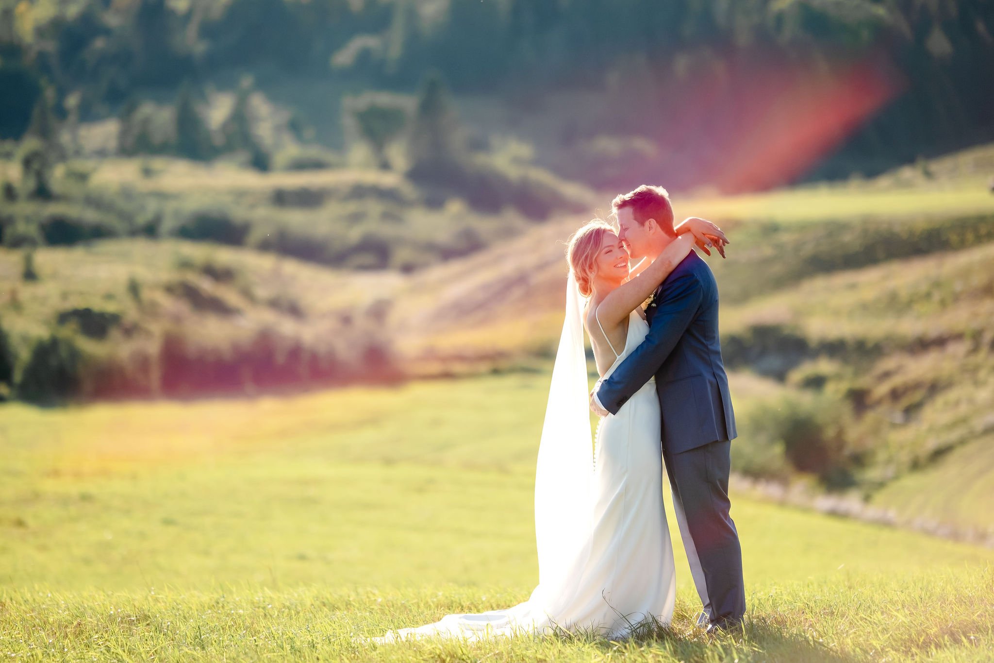 natural light photograph of a bride and groom in front of an expansive field as the sun sets behind them