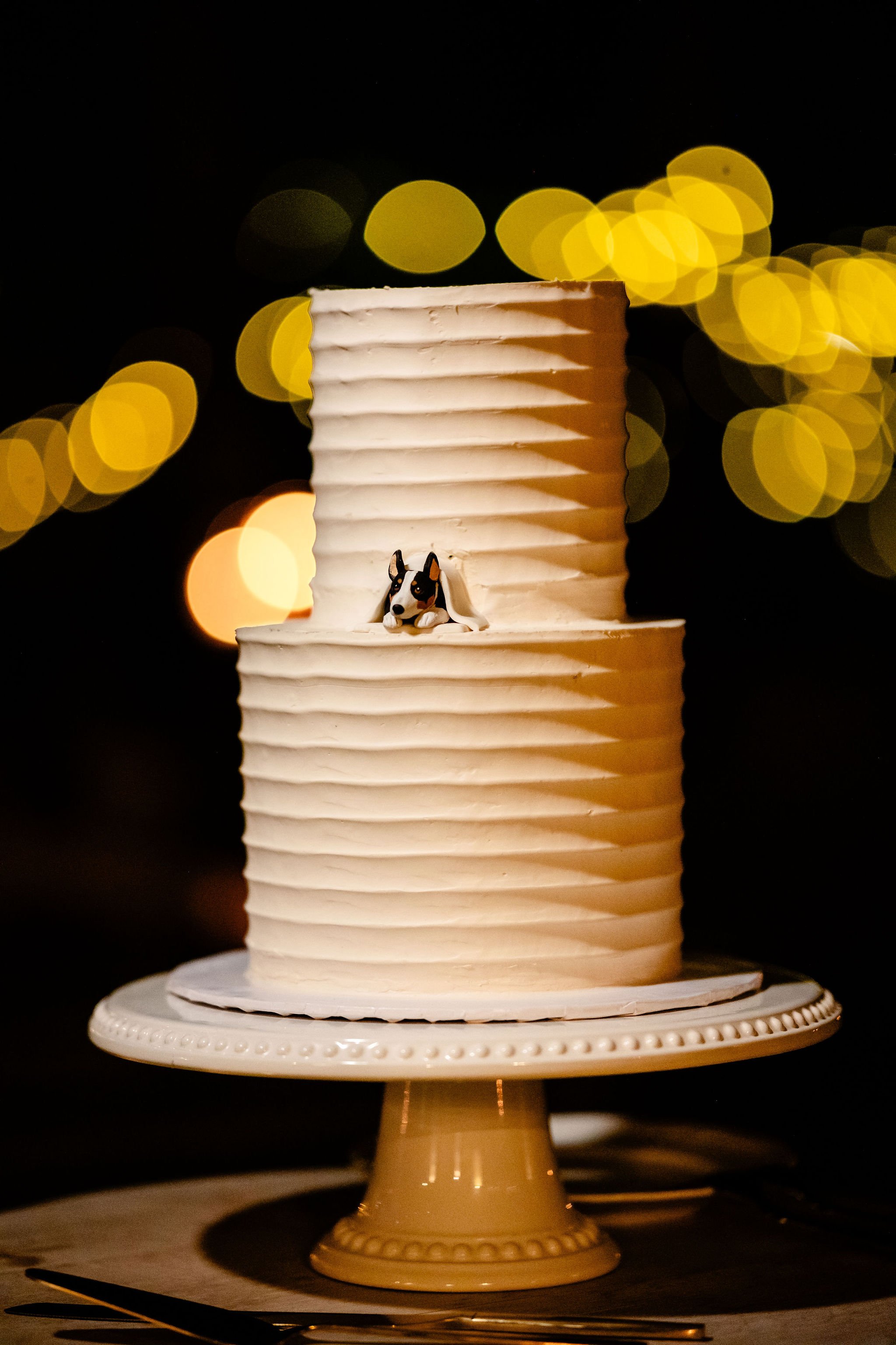 a wedding cake with a little dog peeking out from between the layers