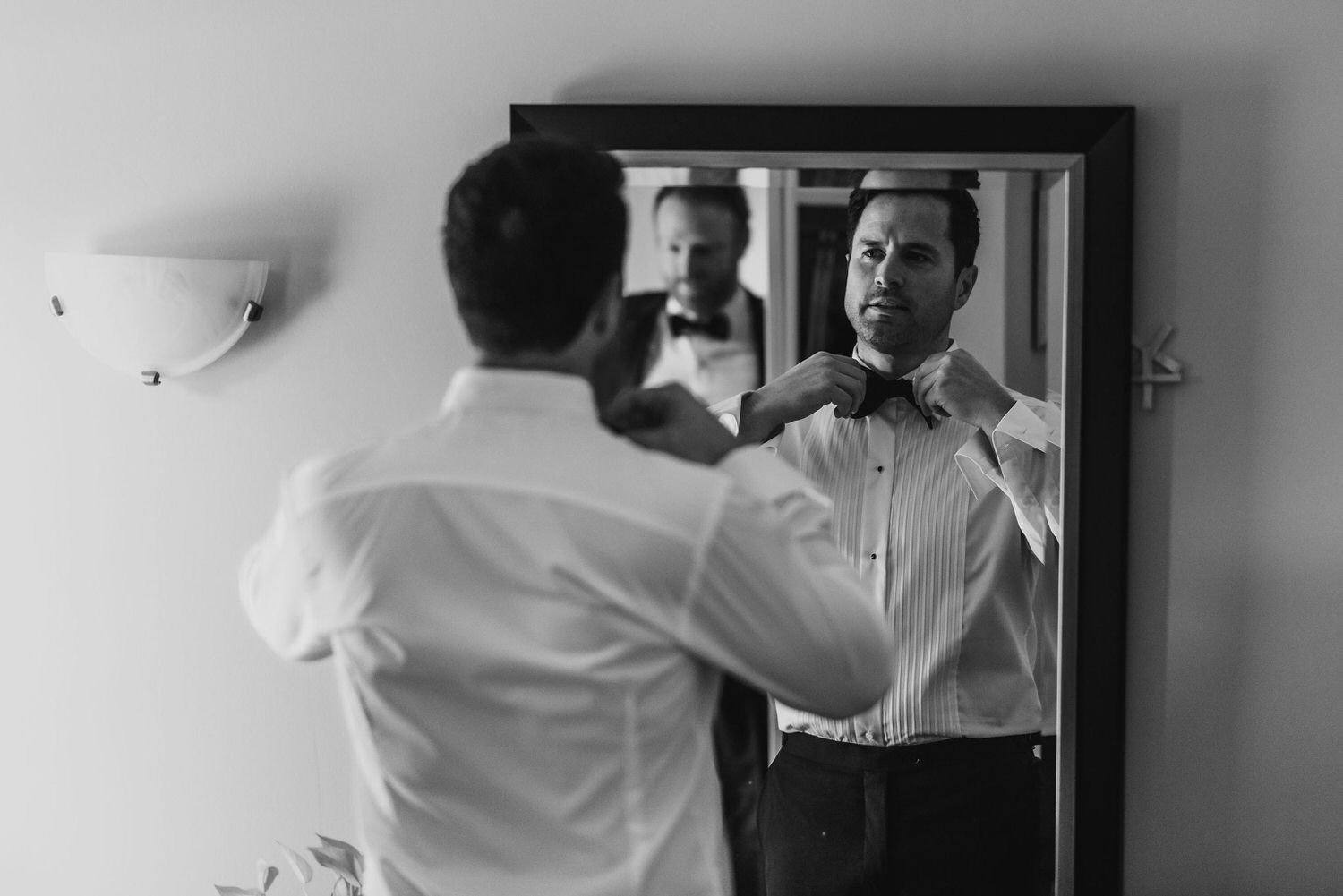 Black and white photograph of a groom putting on a bow tie