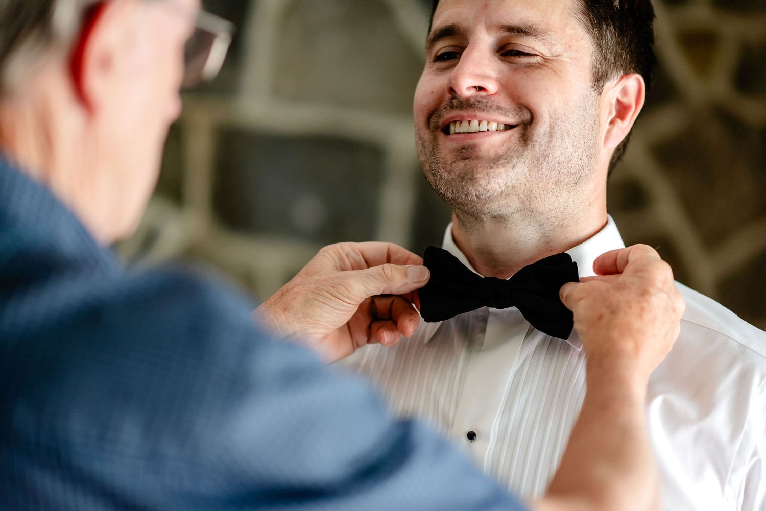 a grooms father helps in him with his bow tie