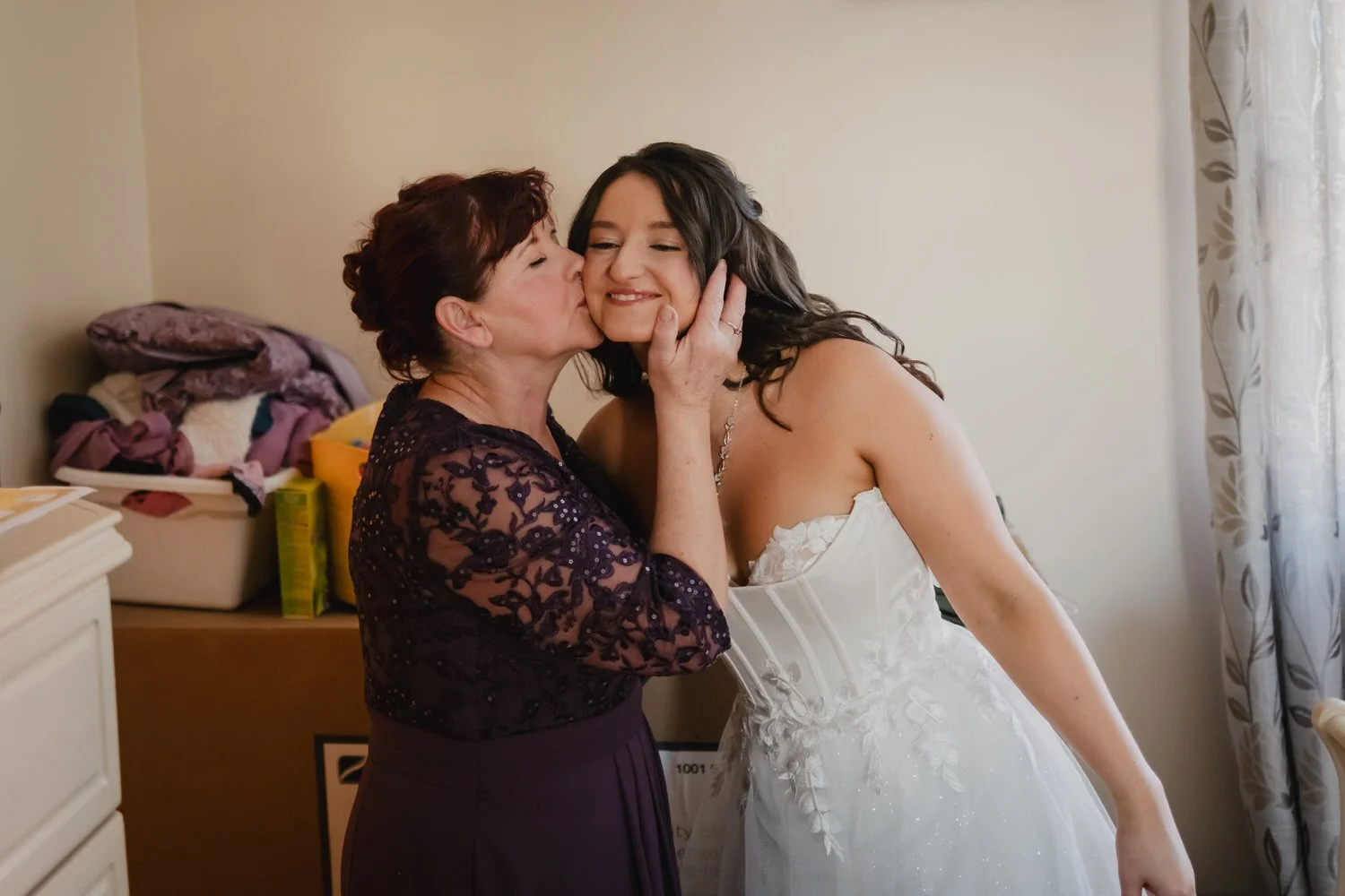 a brides mom kisses her after she puts on her wedding gown