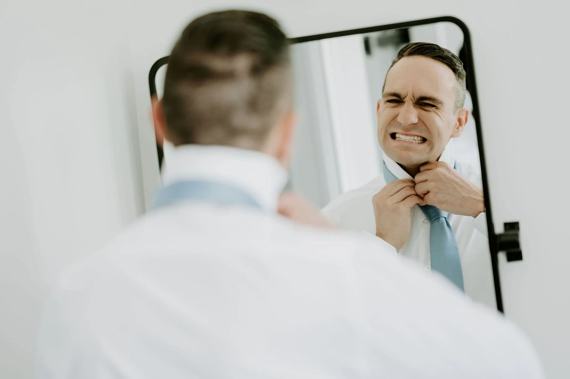 Petar pulling a playful grimace in the mirror while tightening his pale blue tie