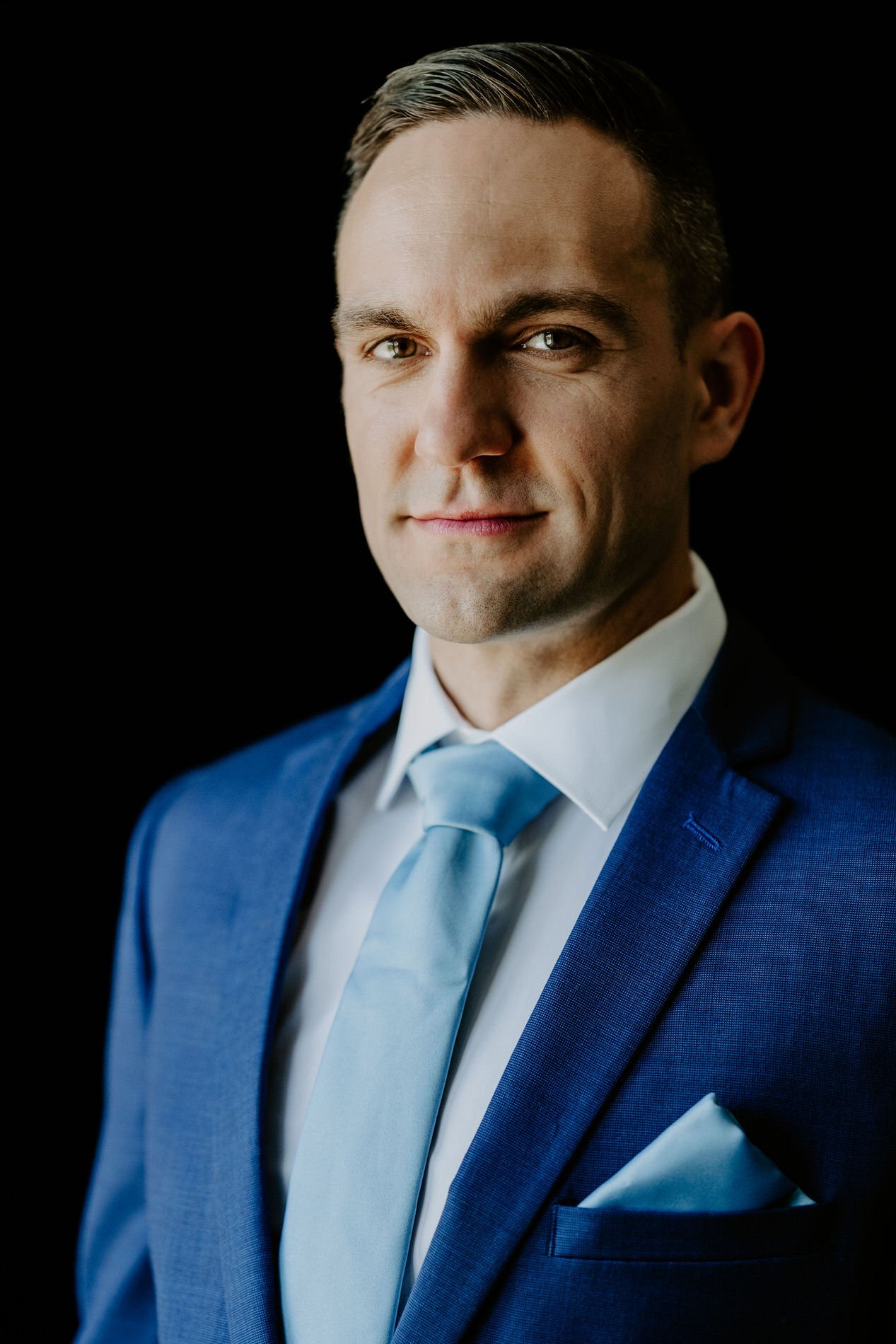 Portrait of the groom, Petar, in a blue suit, pale blue tie and pocket square against a dark background