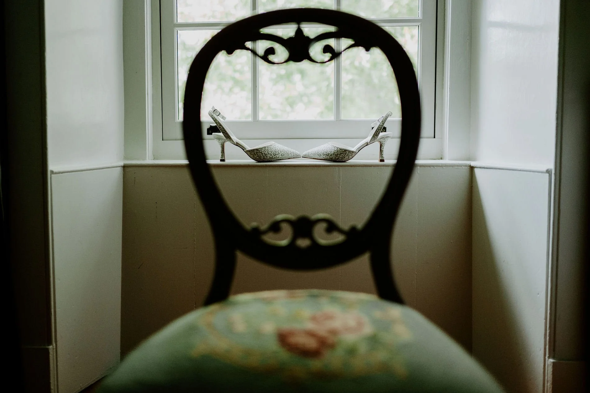 Holly's glittering heels on a windowsill, framed through the carved back of an antique chair