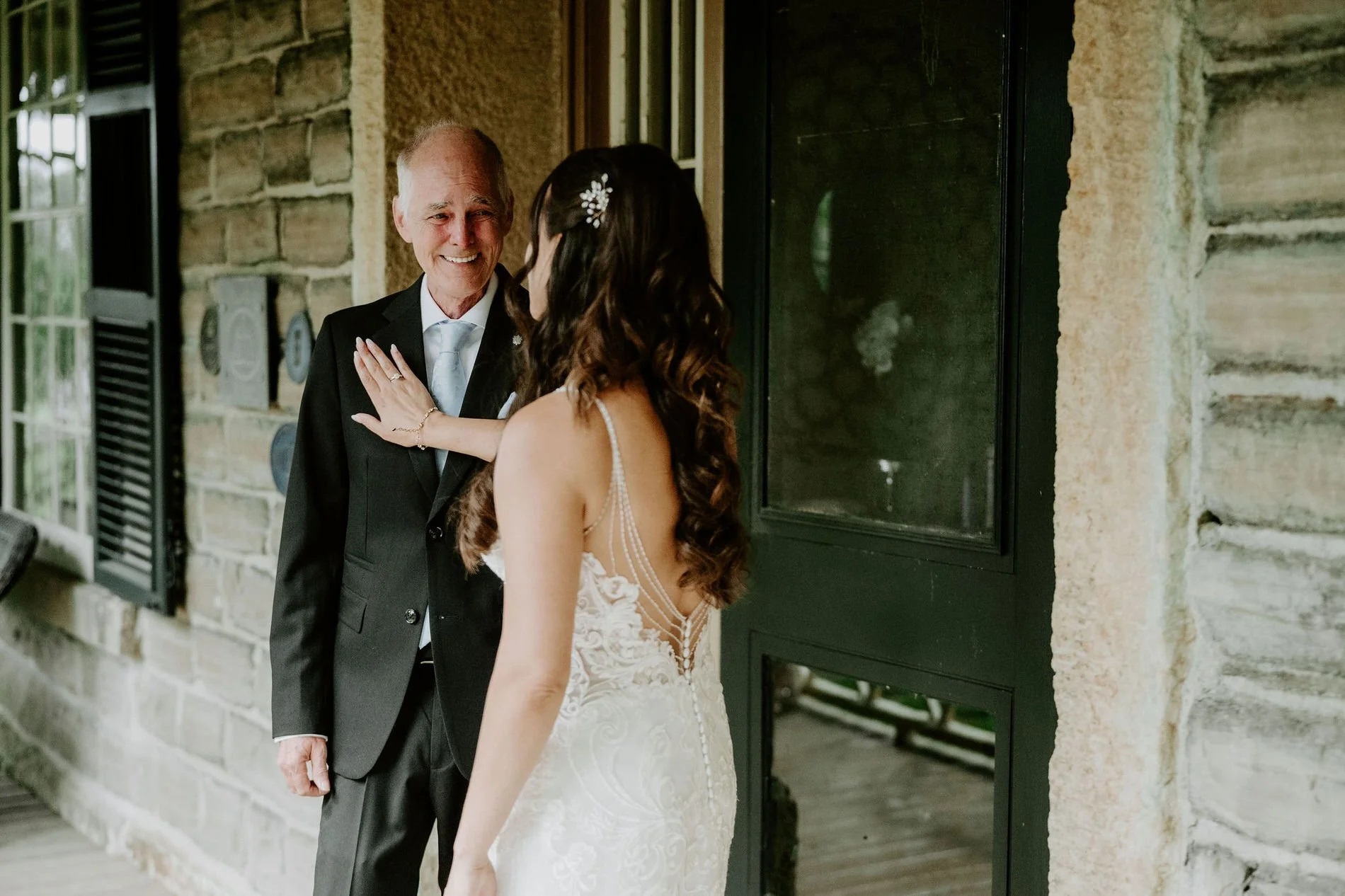 Holly touching her father's lapel as he smiles at her on the porch of the historic stone house at Evermore