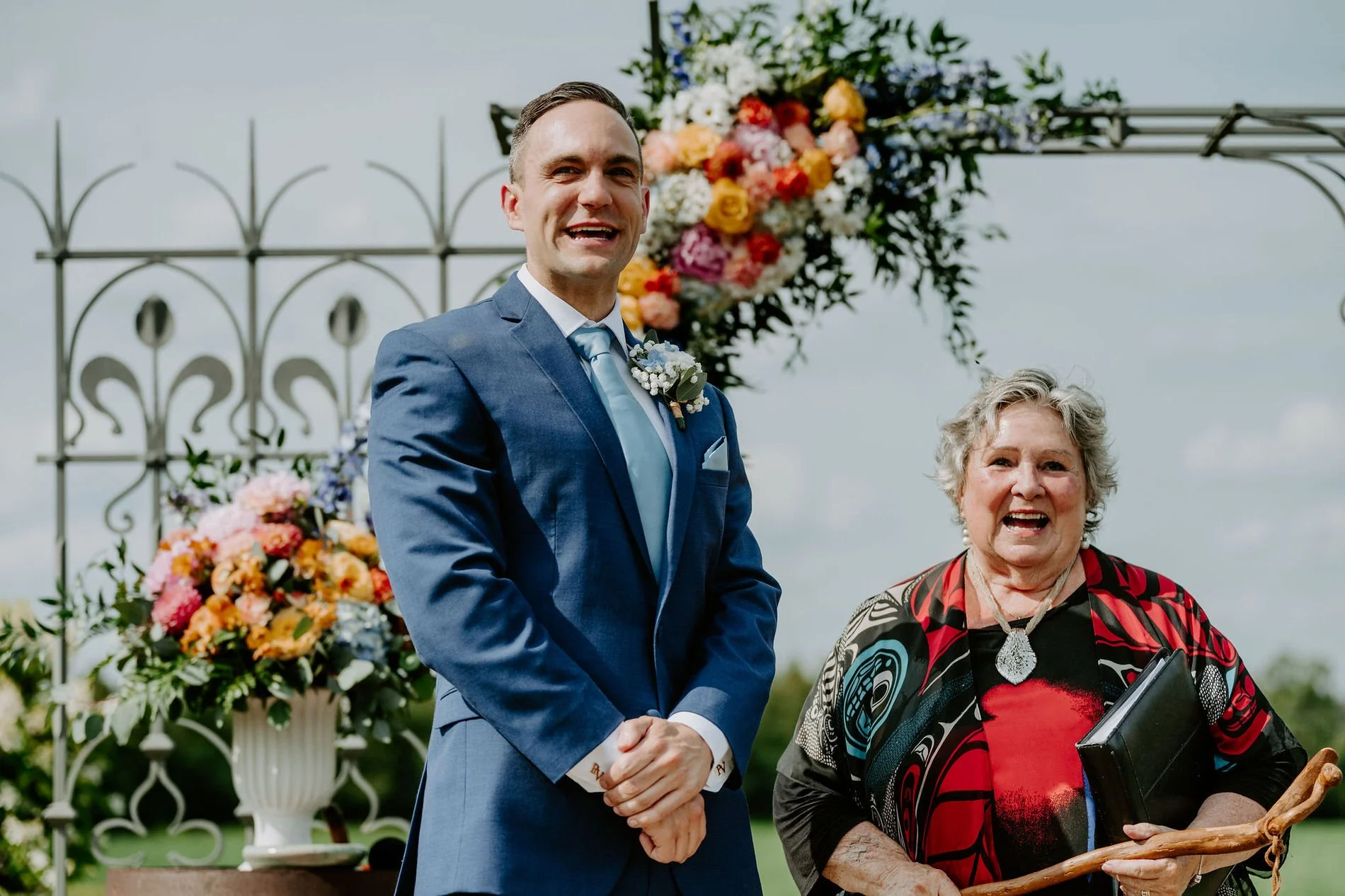 Petar and the officiant laughing beneath a flower-covered wrought-iron arch at Evermore