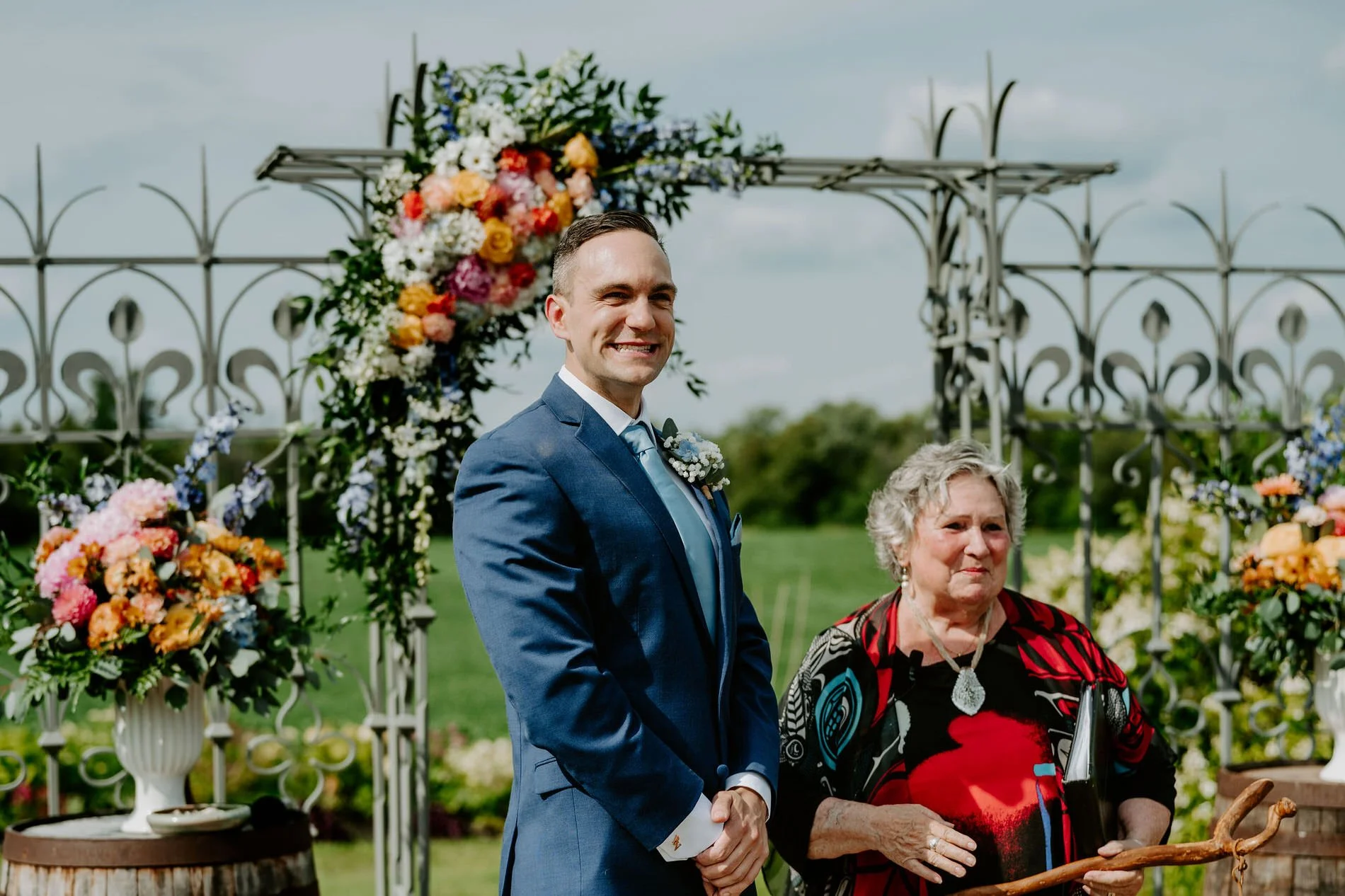 Petar smiling at the altar under a floral arch as he waits for Holly at Evermore