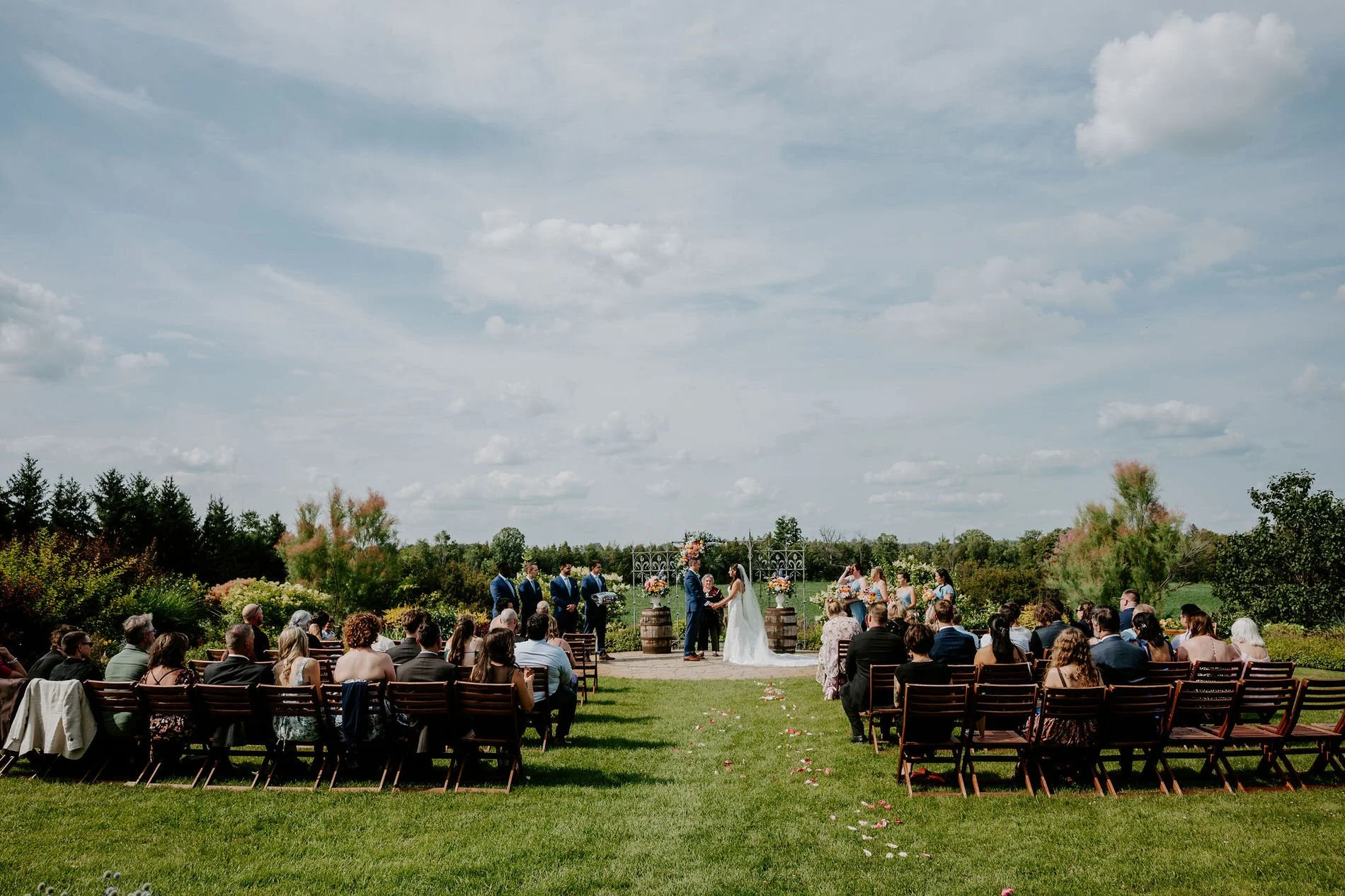 Wide view of Holly and Petar's outdoor ceremony on the lawn at Evermore in Ottawa, under a big cloudy sky