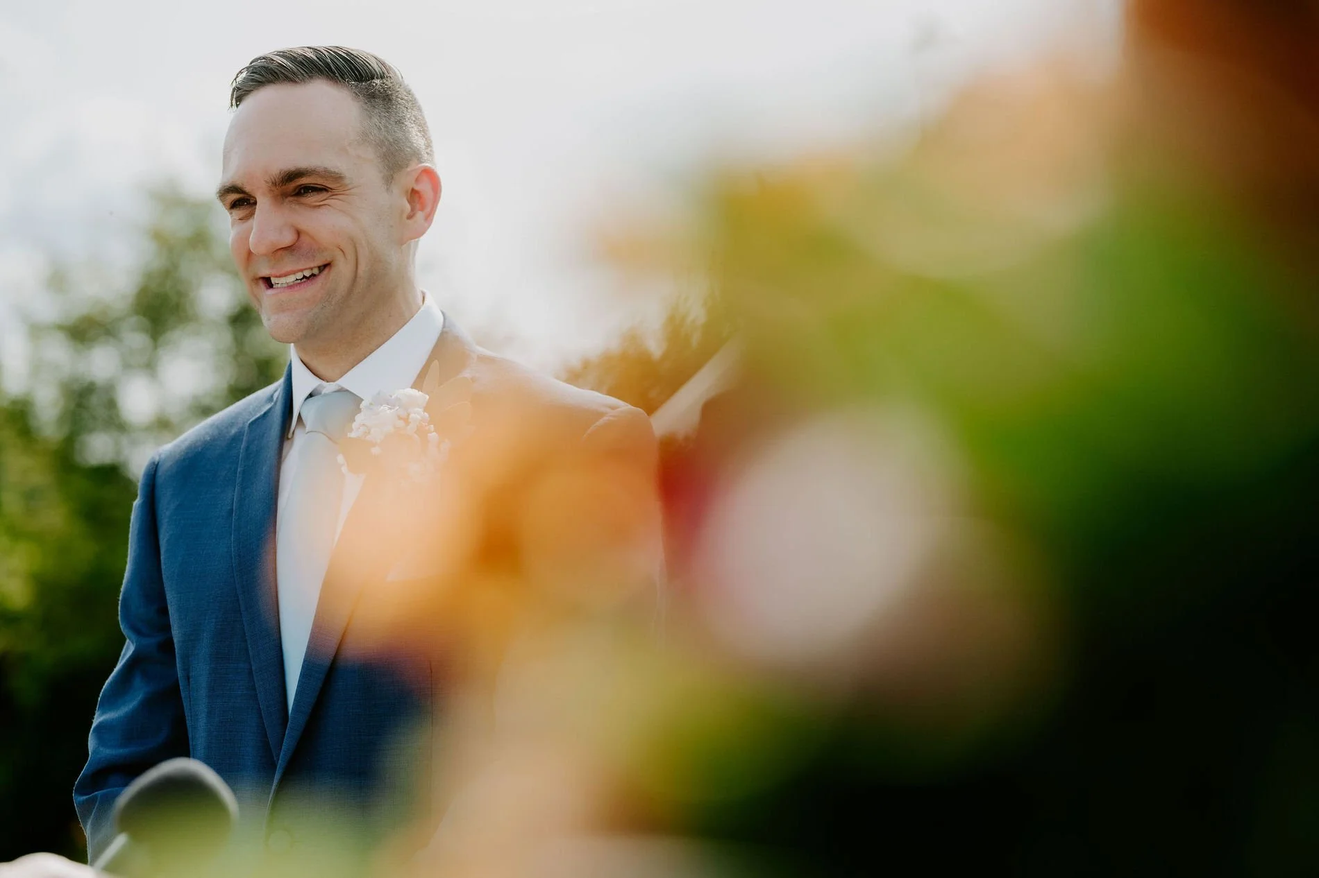 Petar smiling during the ceremony, framed by blurred flowers in the foreground