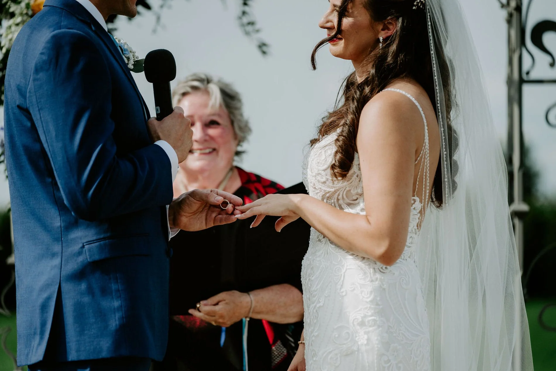 Petar sliding the wedding ring onto Holly's finger as the officiant smiles behind them