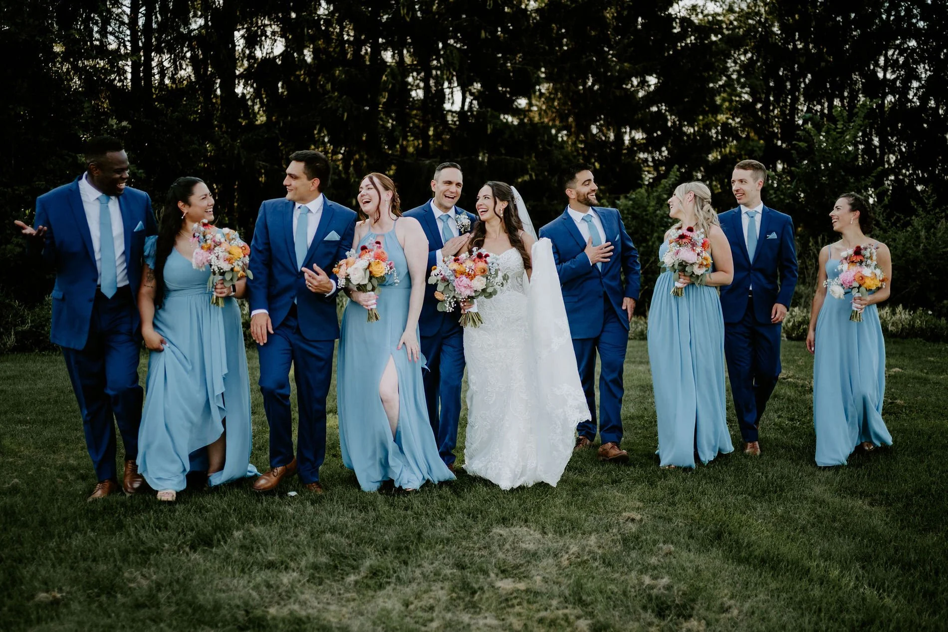 Holly and Petar's wedding party walking across the lawn at Evermore, groomsmen in blue and bridesmaids in dusty blue