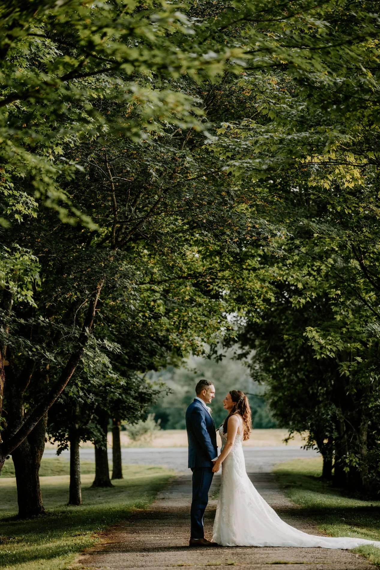Holly and Petar facing each other on a lane beneath a canopy of tall trees at Evermore in Ottawa