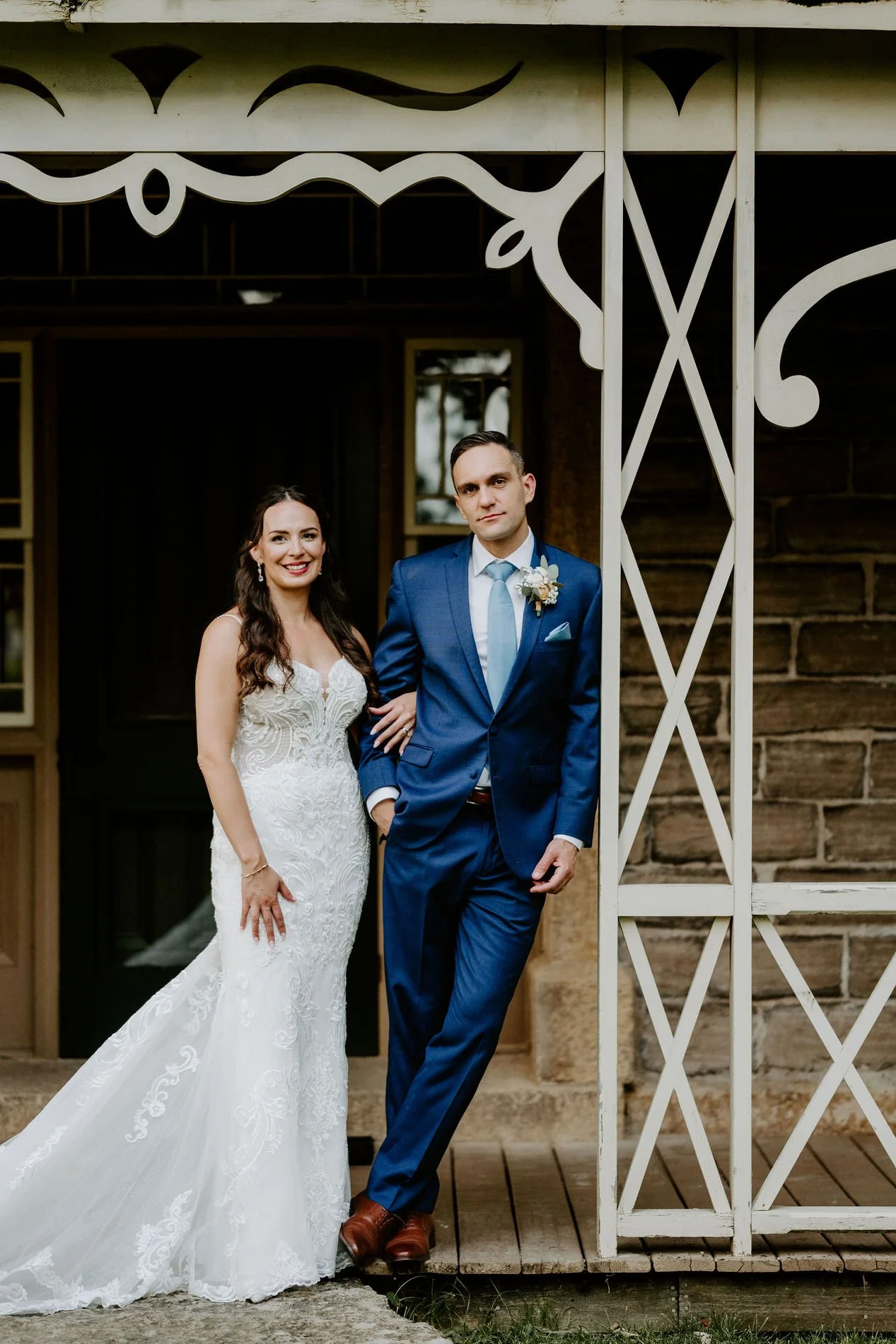 Holly and Petar arm in arm on the white lattice porch of the stone house at Evermore