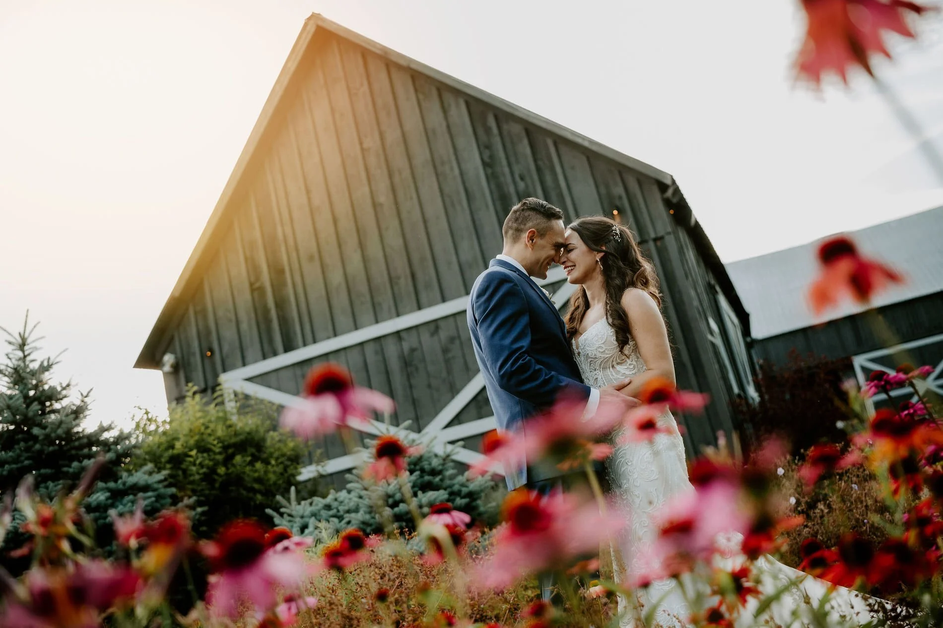 Holly and Petar resting their foreheads together in front of the weathered grey barn at Evermore
