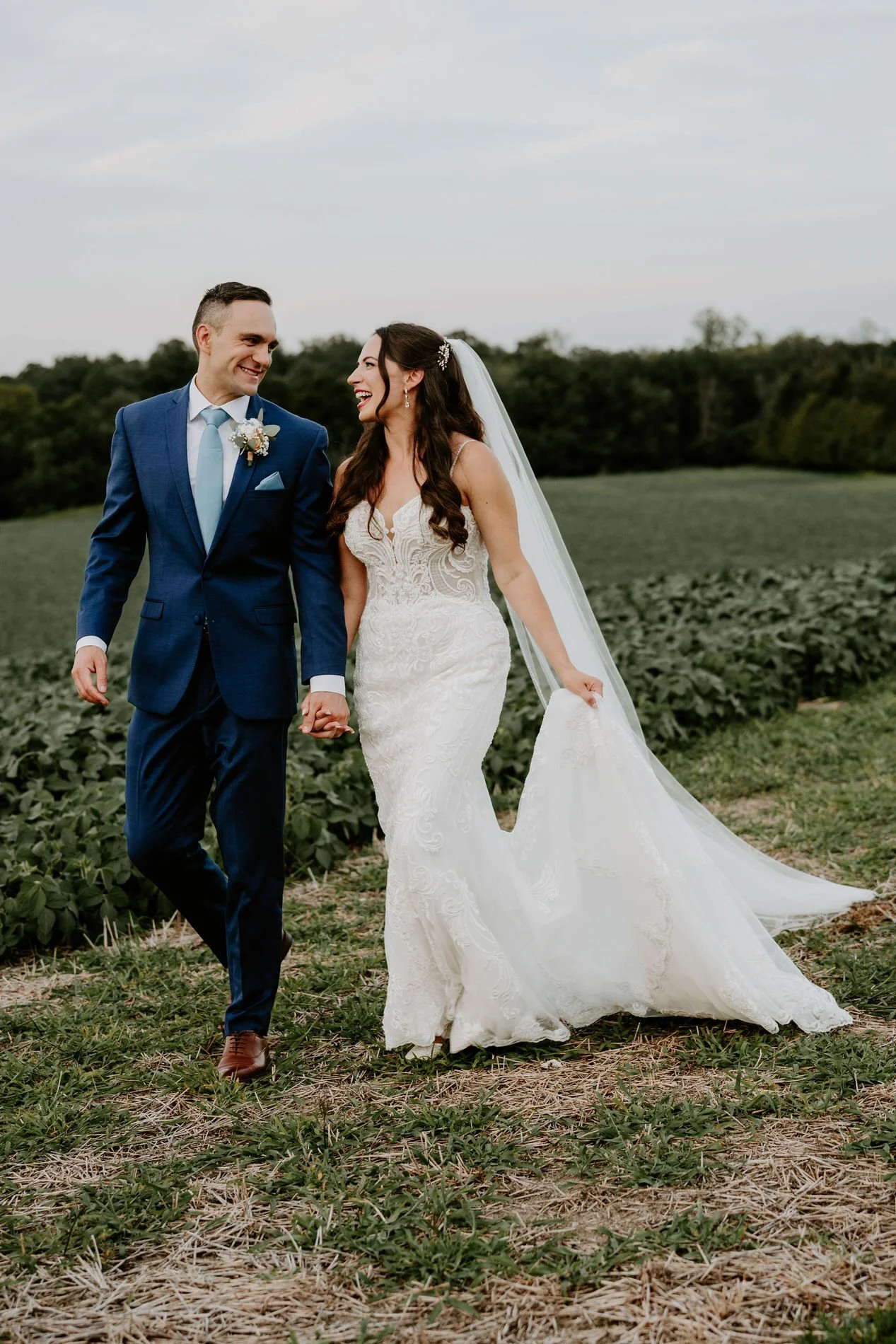 Holly laughing as she walks hand in hand with Petar through the fields at Evermore at dusk
