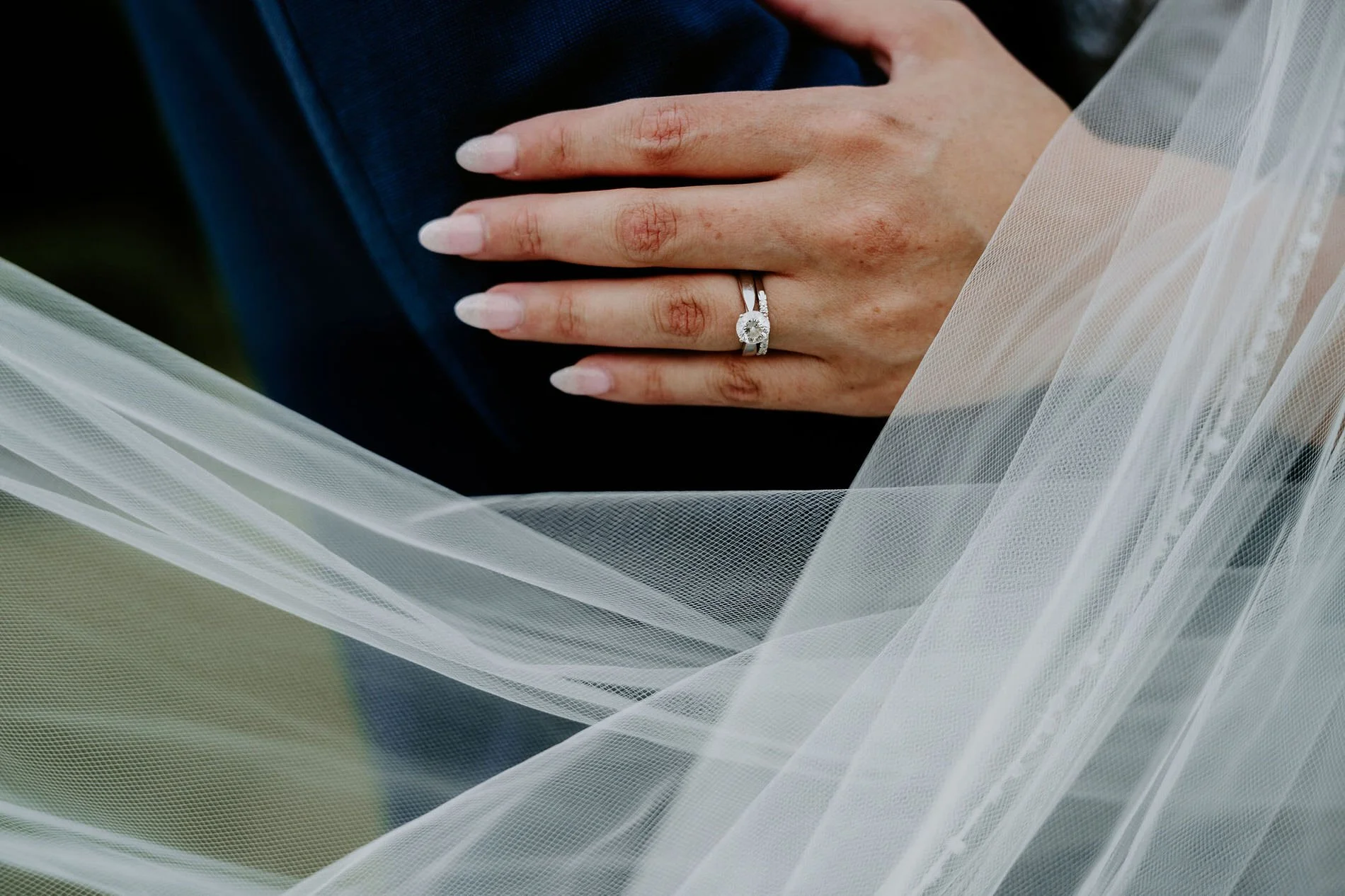 Close-up of Holly's engagement ring and wedding band as her hand rests on Petar's jacket