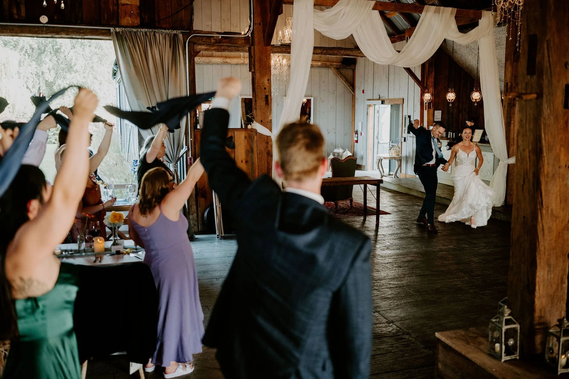 Holly and Petar's grand entrance into the rustic barn at Evermore as guests wave napkins overhead
