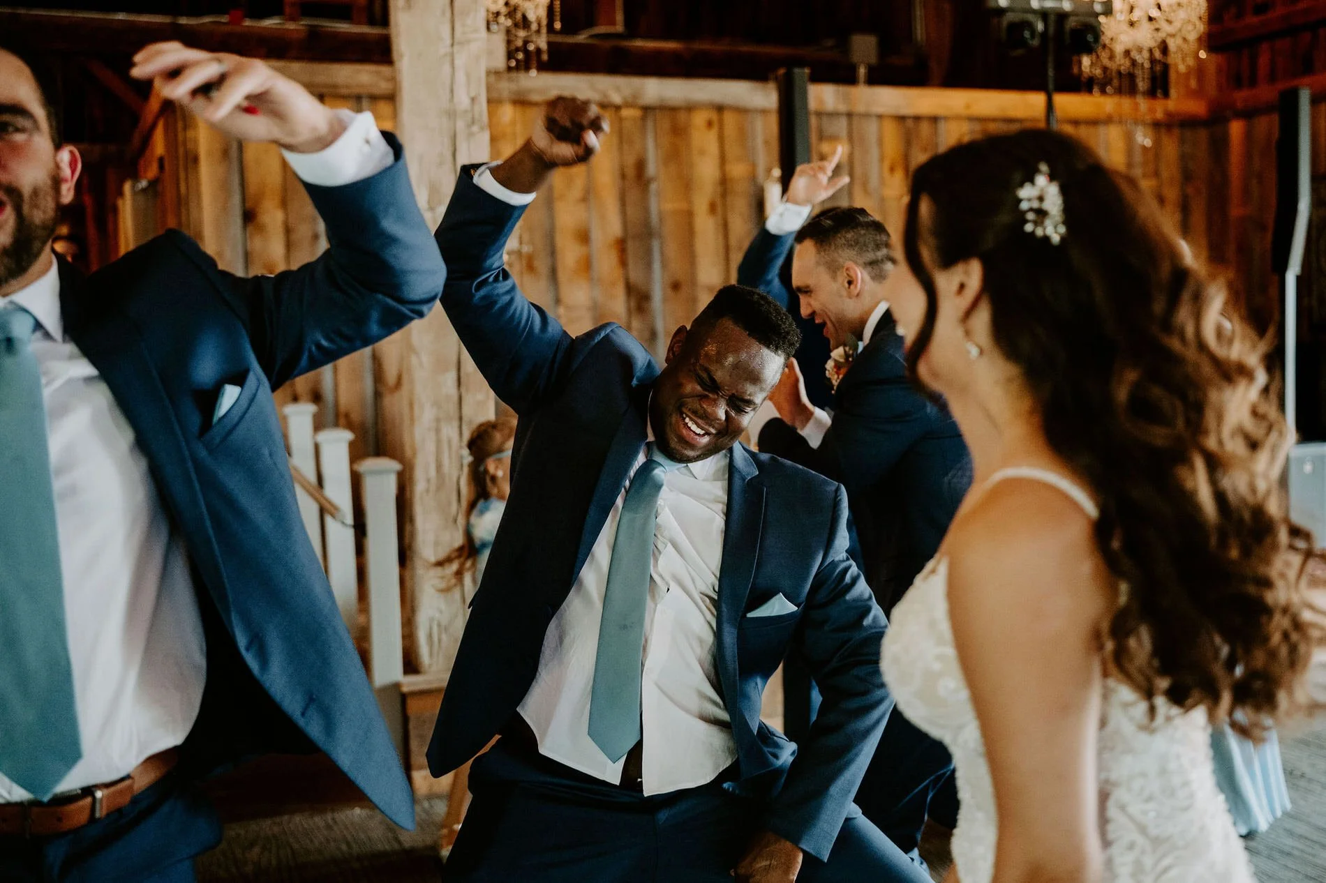 Groomsmen dancing enthusiastically with arms raised around Holly at the reception