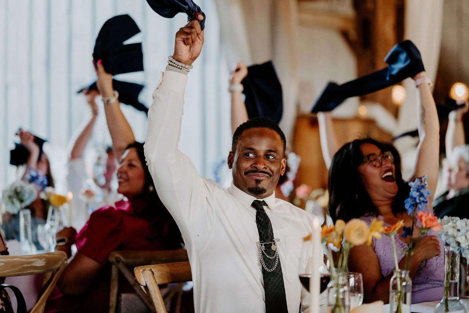 Cheering guests waving napkins over their heads at the reception tables in the barn at Evermore